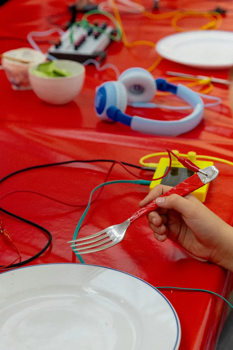 Atelier sonore : fourchette branchée sur une table rouge, casque audio